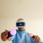 Person enjoying a virtual reality game with VR goggles and interactive controllers indoors.