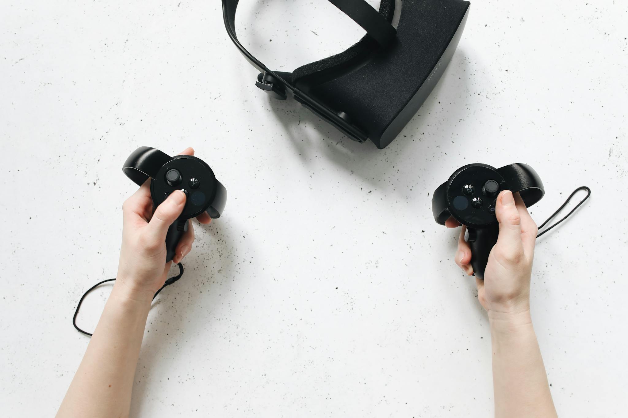 Two hands hold virtual reality controllers above a VR headset, showcasing modern technology.
